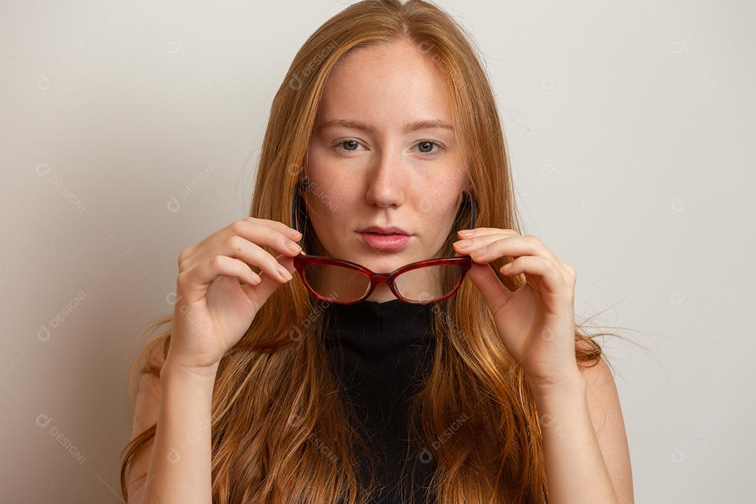 Linda jovem ruiva garota de óculos está olhando para a câmera