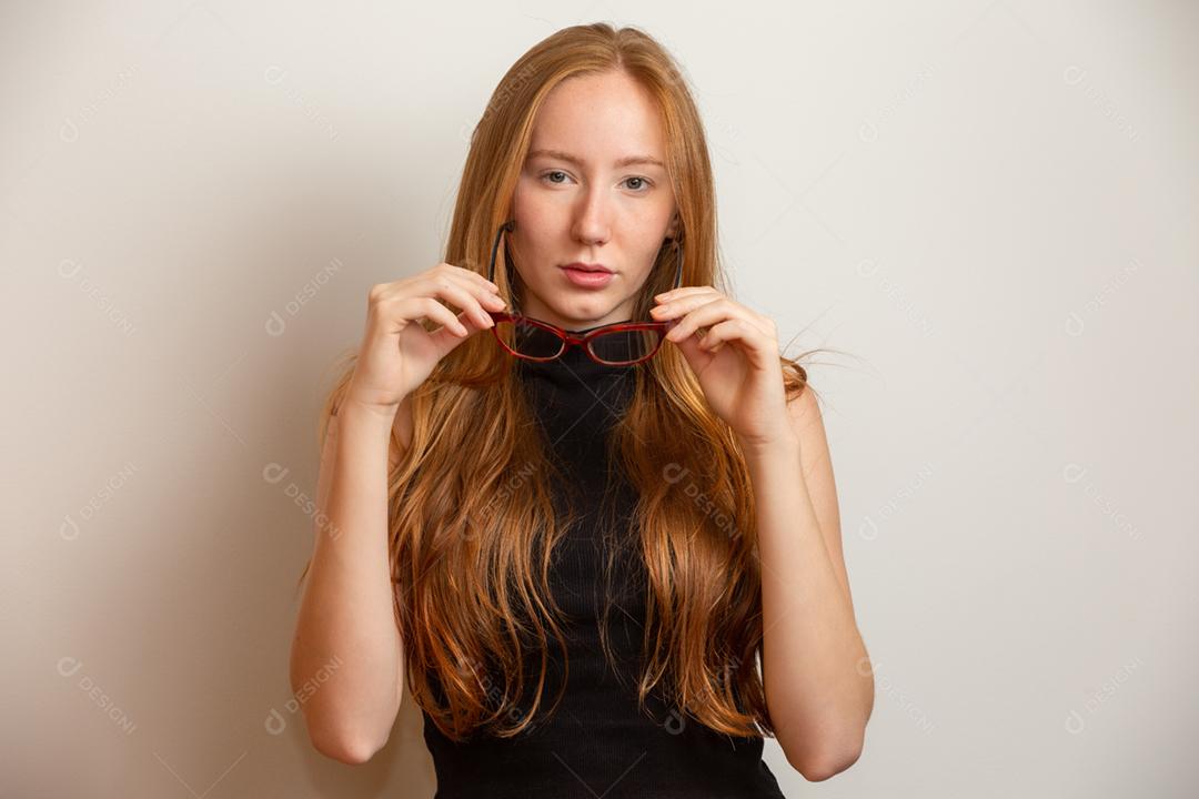 Linda jovem ruiva de óculos está olhando para a câmera e sorrindo, sobre fundo cinza.