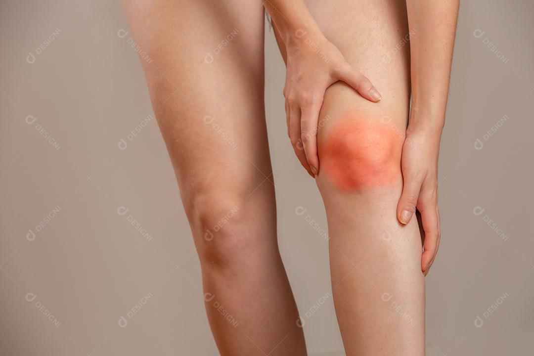 Dor óssea ou joelhos ao redor do joelho. A mão da garota está segurando a área do joelho. Mulher ruiva.