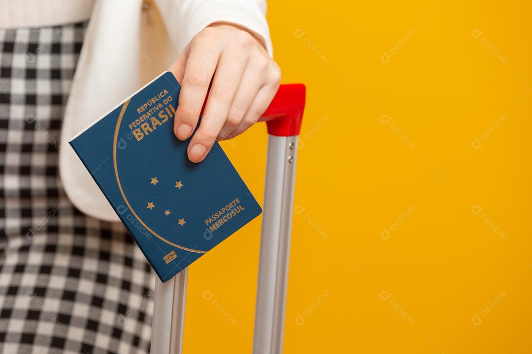 Closeup mão de menina segurando um passaporte brasileiro. Em amarelo.