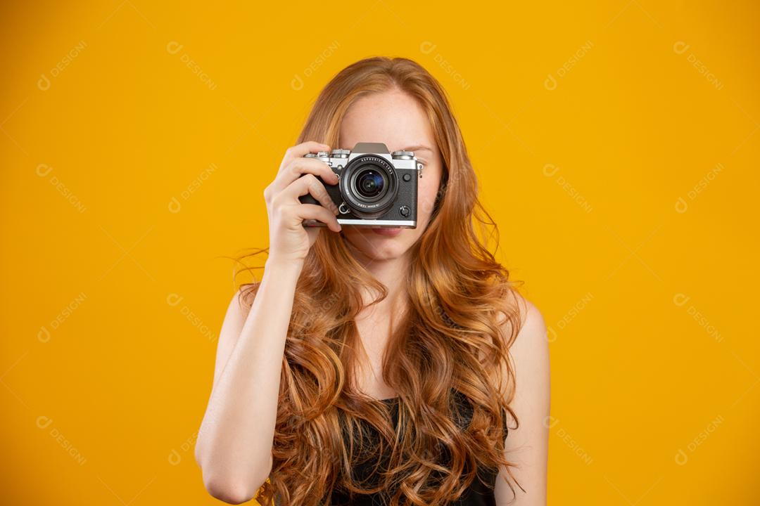 Foto de mulher ruiva adorável vestindo roupas pretas, segurando a câmera vintage retrô e tirando foto