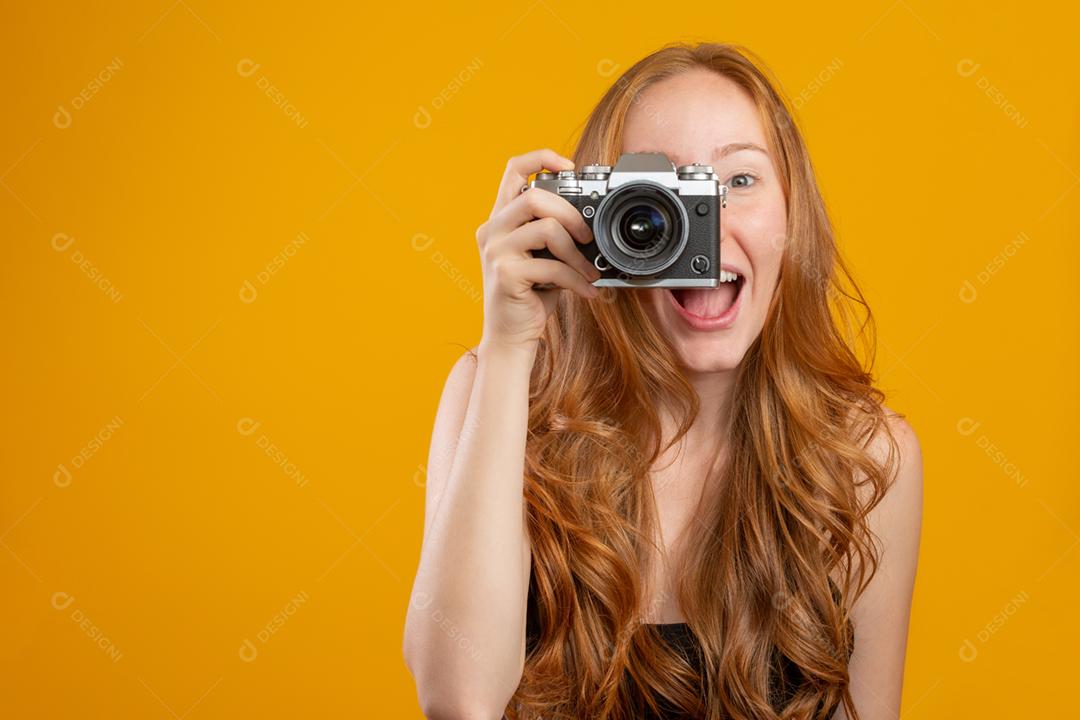 Foto de mulher ruiva adorável vestindo roupas pretas, segurando a câmera vintage retrô e tirando foto