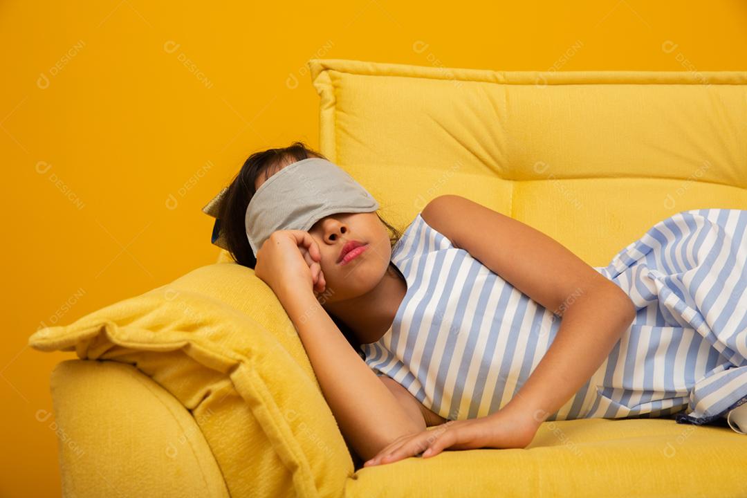 Criança asiática dormindo em um sofá com máscara de dormir.