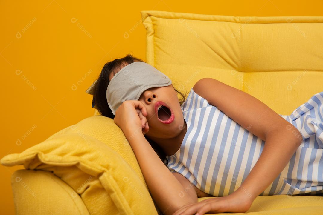 Criança asiática dormindo em um sofá com máscara de dormir.