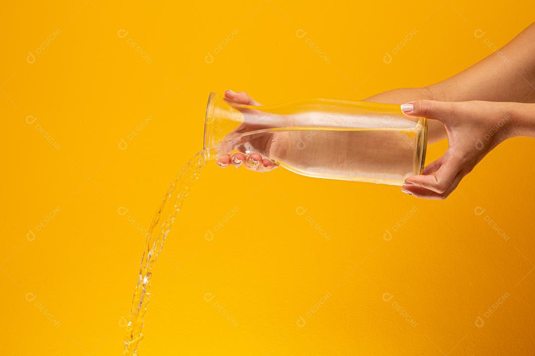 Despeje a água no vidro. Derramamento de água. Salpicos de água no fundo amarelo.