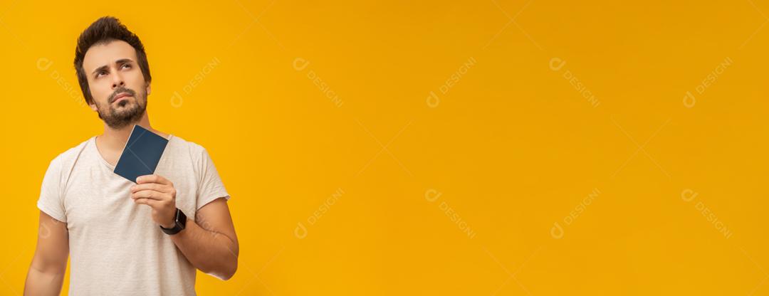 Jovem segurando um passaporte, cartão de trabalho ou documento, pensando. Em fundo amarelo