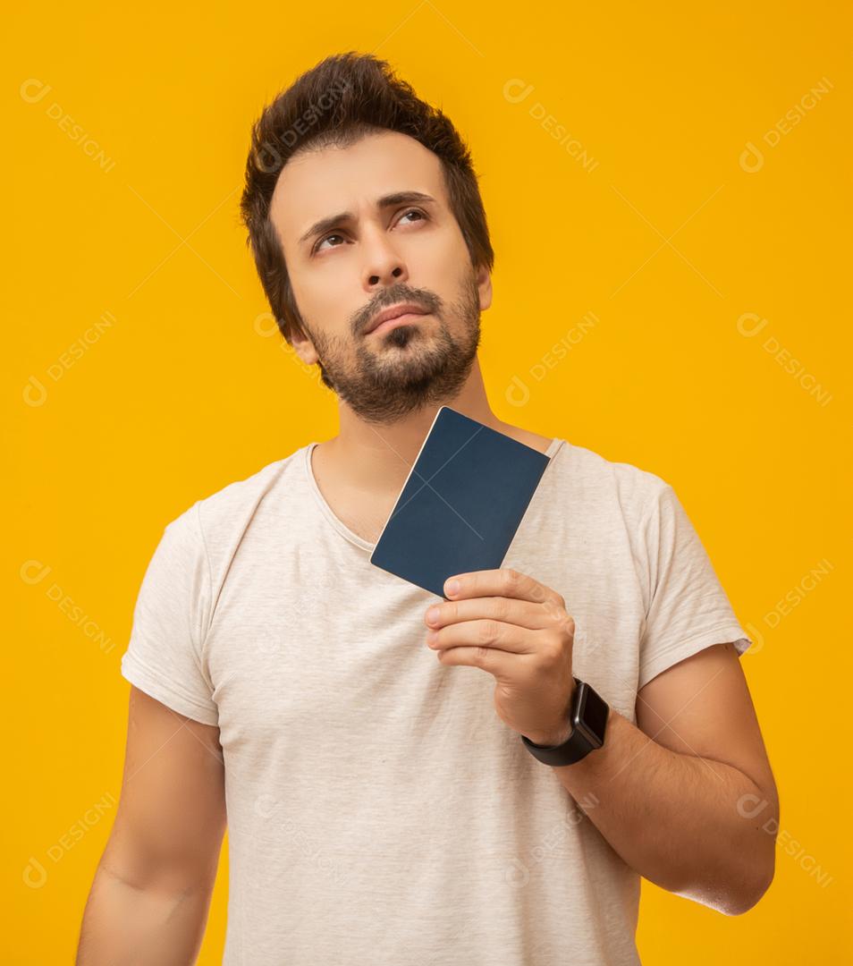 Jovem segurando um passaporte, cartão de trabalho ou documento, pensando. Em fundo amarelo