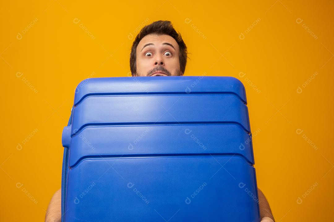 Homem engraçado segurando uma mala de viagem pesada. Em fundo amarelo