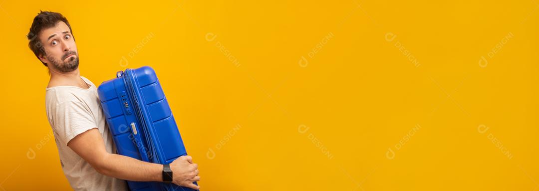 Funny man holding a heavy travel bag. On yellow background