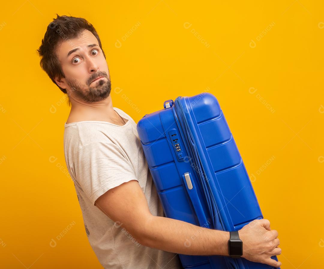 Homem engraçado segurando uma mala de viagem pesada. Em fundo amarelo