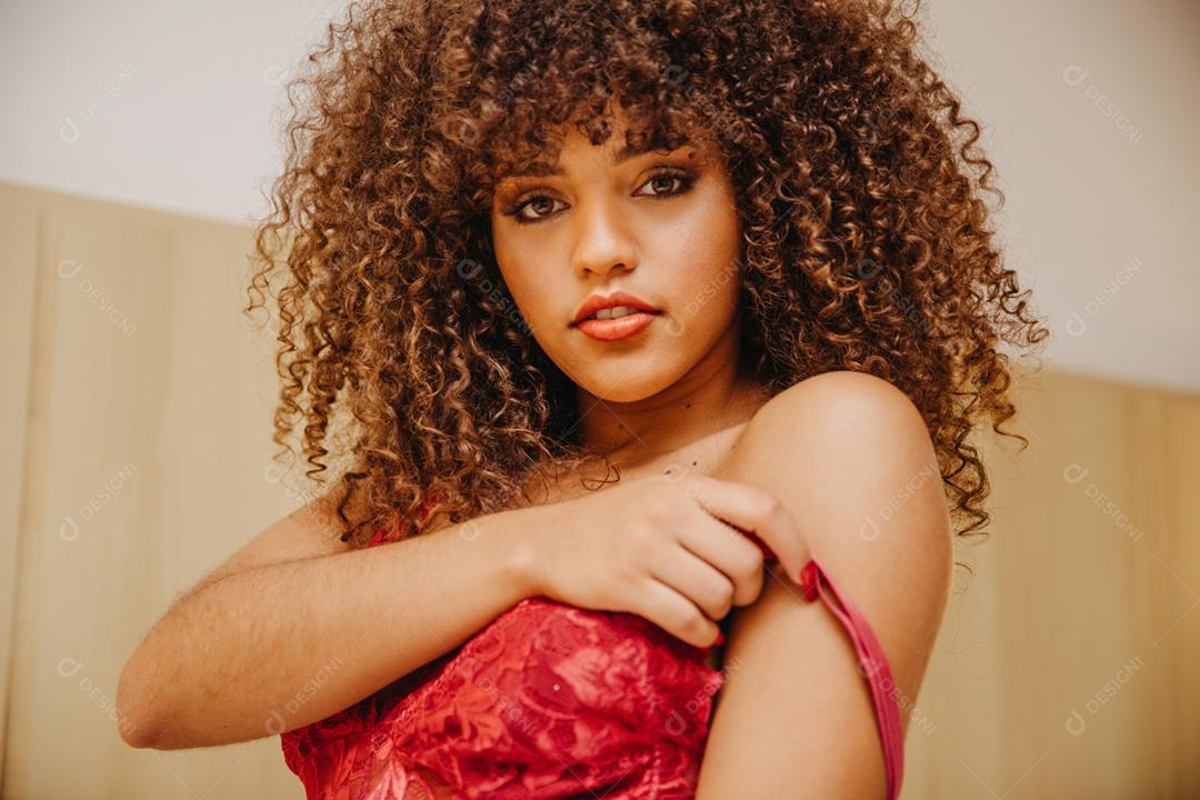 Mulher jovem e bonita com cabelos cacheados em lingerie sexy e sensual em uma cama posando para a câmera