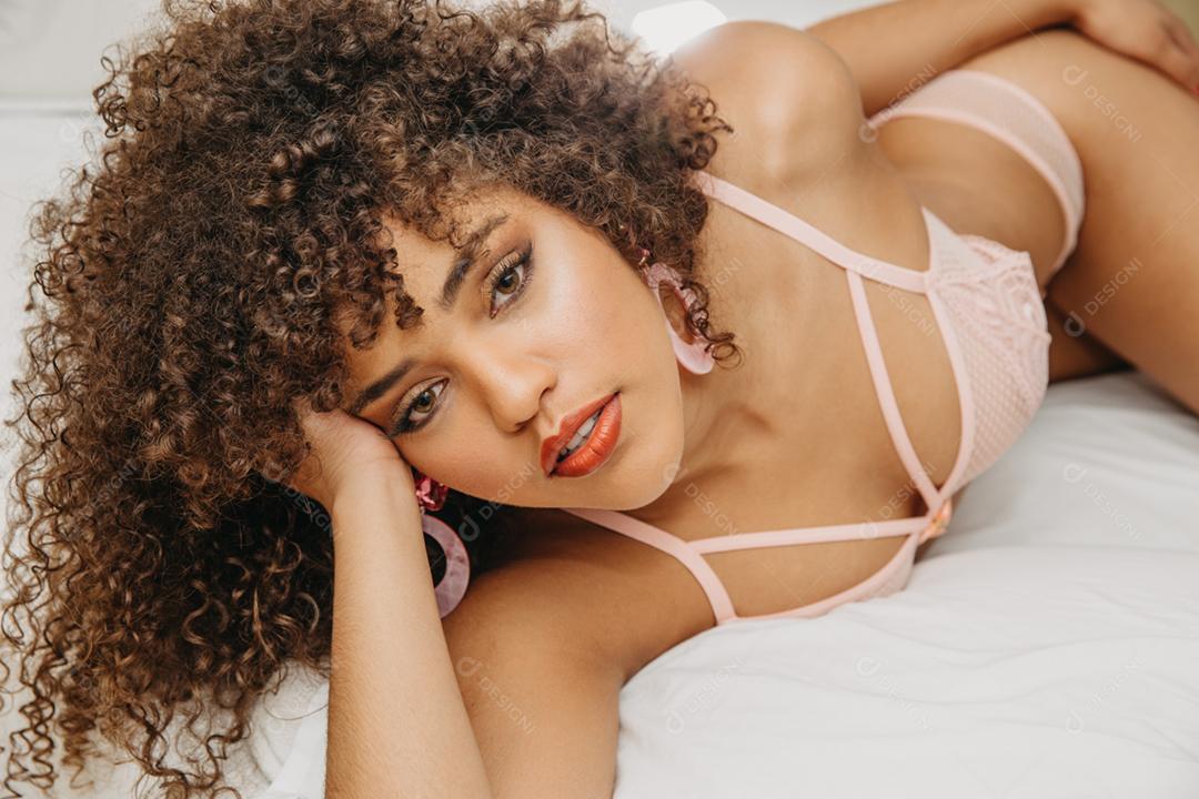 Mulher jovem e bonita com cabelos cacheados em lingerie sexy e sensual em uma cama posando para a câmera