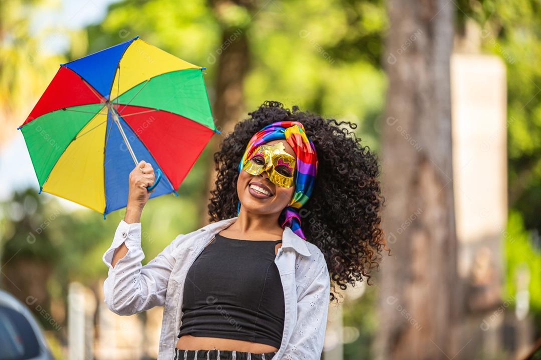 Mulher jovem de cabelo encaracolado comemorando a festa de carnaval brasileira com guarda-chuva de Frevo na rua.