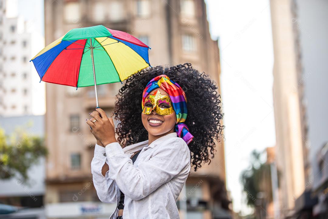 Mulher jovem de cabelo encaracolado comemorando a festa de carnaval brasileira com guarda-chuva de Frevo na rua.