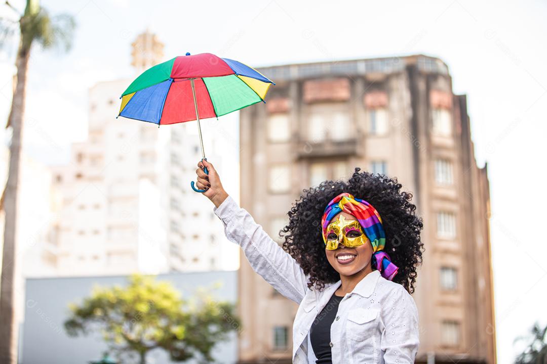 Festa carnavalesca. Mulher brasileira de cabelo encaracolado fantasiada soprando confete
