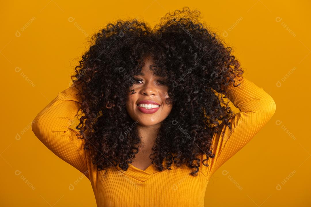 Jovem afro-americana com cabelos cacheados, olhando para a câmera e sorrindo. Linda garota