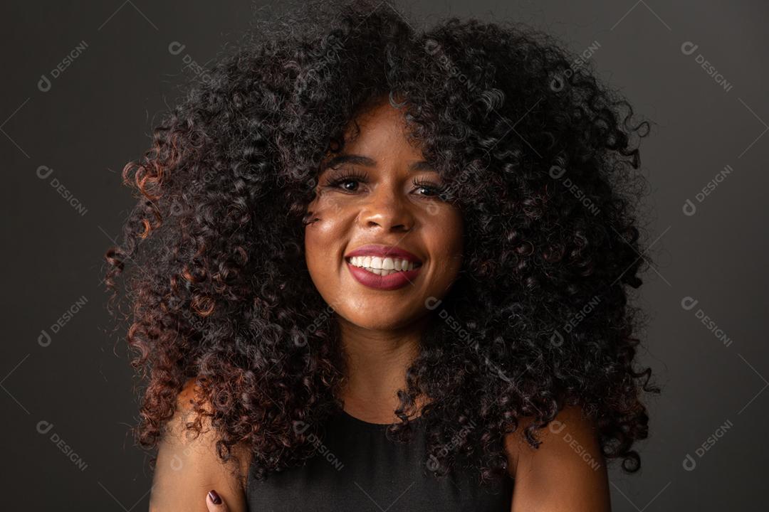 Jovem afro-americana com cabelos cacheados, olhando para a câmera e sorrindo. Linda garota