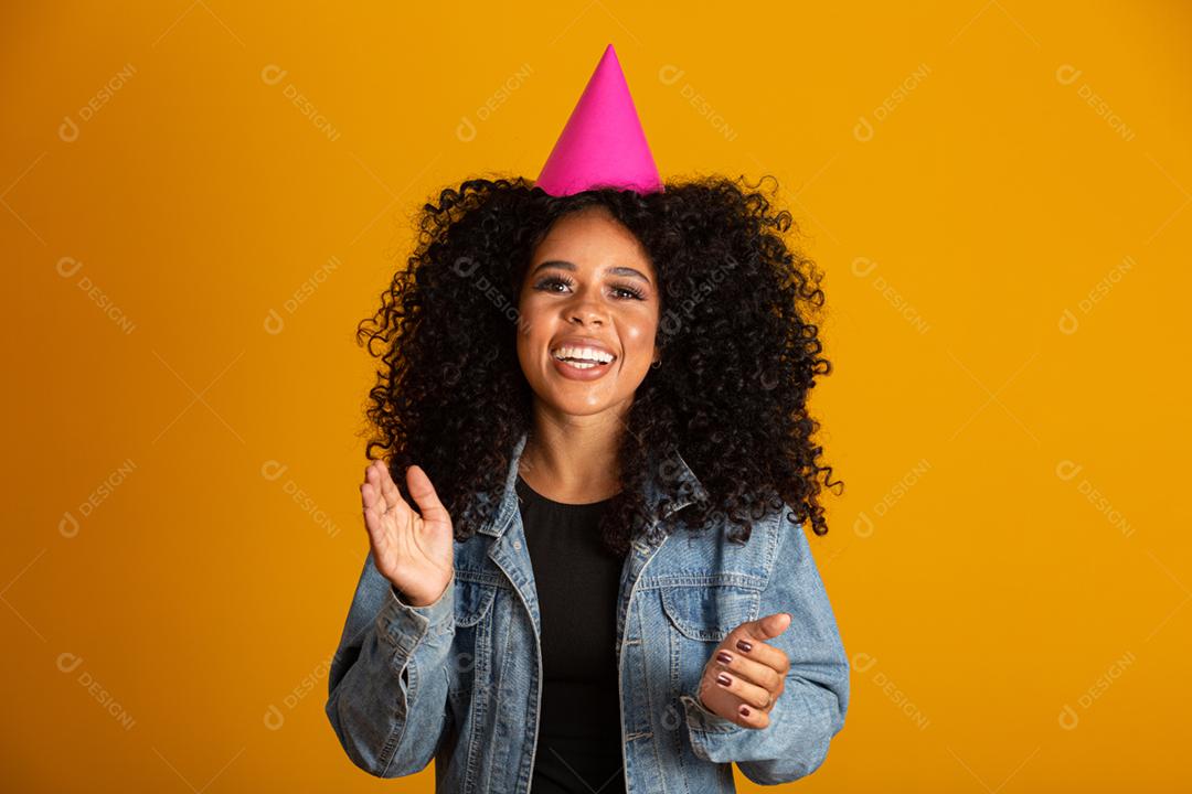 Jovem mulher afro-americana usando chapéu de aniversário sobre fundo amarelo isolado