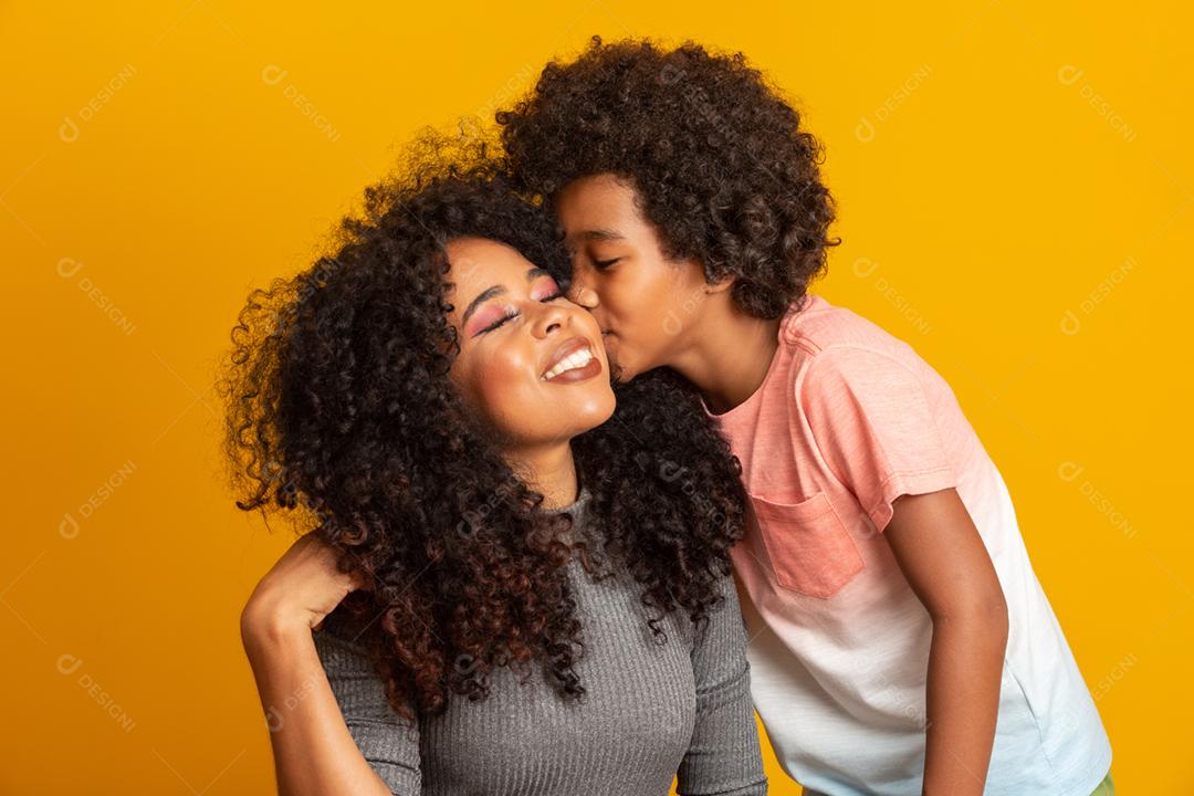 Retrato de jovem mãe afro-americana com filho da criança. Filho beijando sua mãe. Fundo amarelo