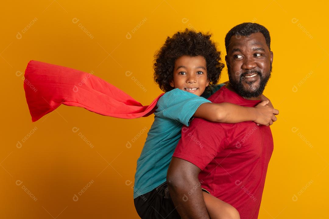 Africano pai e filho jogando super-herói na hora do dia. Pessoas se divertindo fundo amarelo