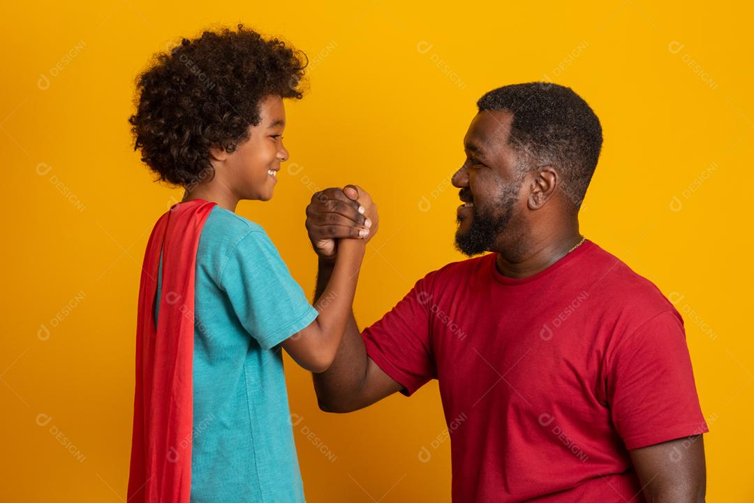 Africano pai e filho jogando super-herói na hora do dia. Pessoas se divertindo fundo amarelo