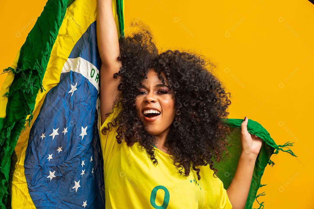 Garota afro torcendo pelo time brasileiro favorito, segurando a bandeira nacional em fundo amarelo.