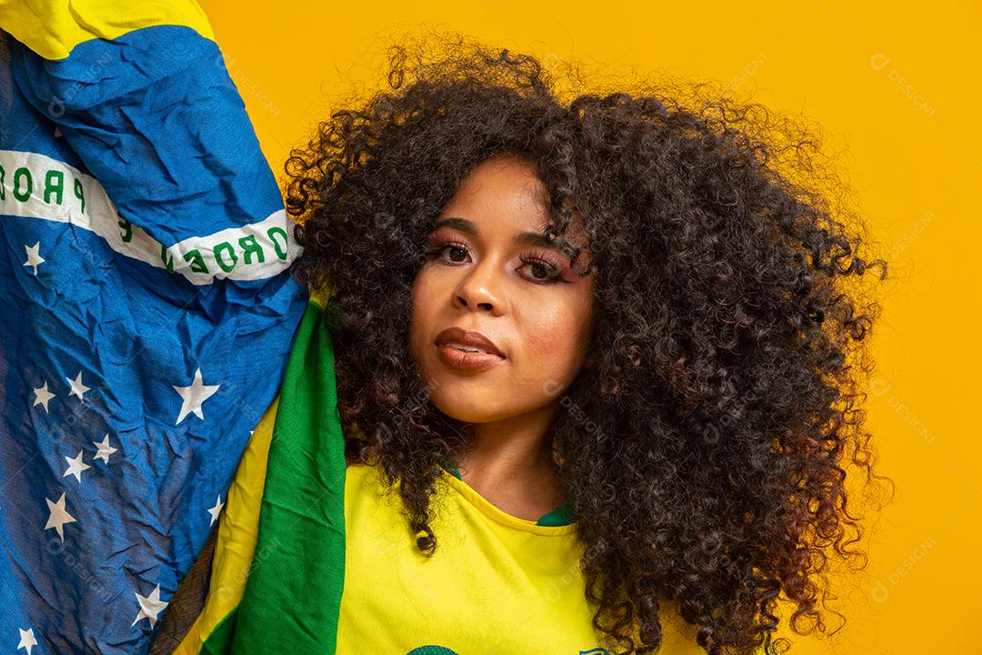 Garota afro torcendo pelo time brasileiro favorito, segurando a bandeira nacional em fundo amarelo.