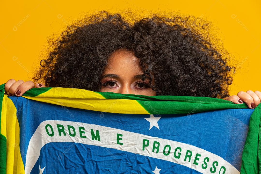 Garota afro torcendo pelo time brasileiro favorito, segurando a bandeira nacional em fundo amarelo.