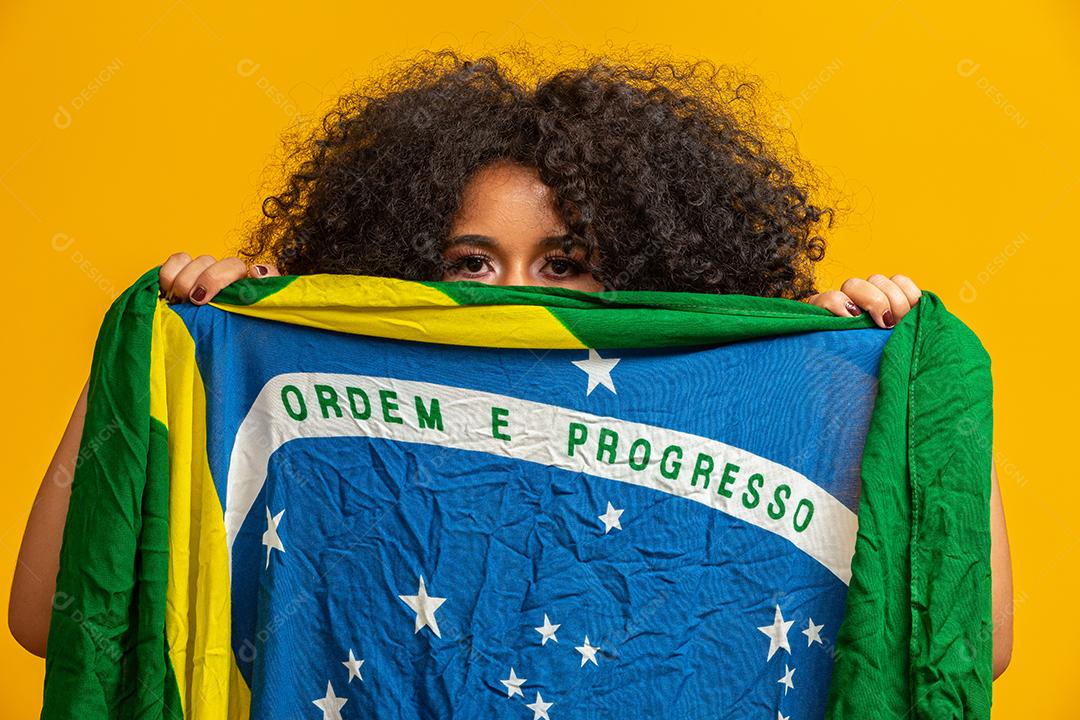 Fã negra misteriosa segurando uma bandeira do Brasil na sua cara. Cores do Brasil