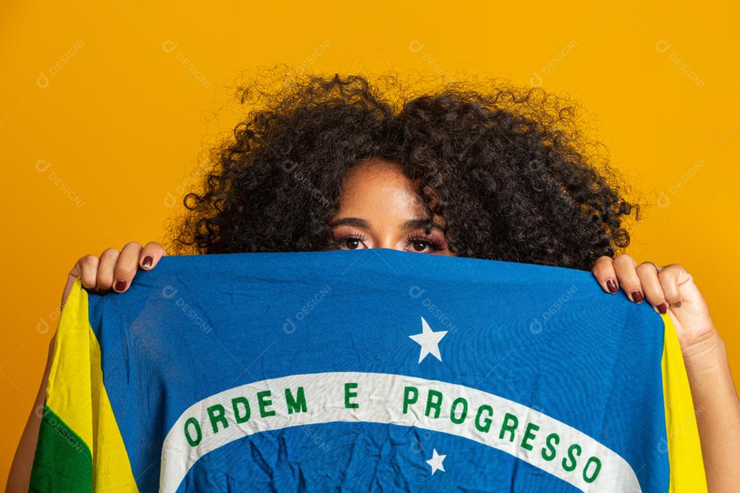 Fã morena misteriosa segurando uma bandeira do Brasil na sua cara. Cores do Brasil ao fundo, verde