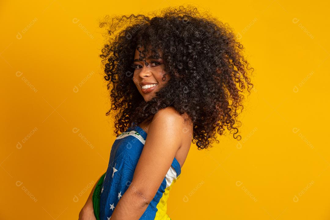 Fã de mulher negra feliz segurando uma bandeira brasileira. Cores do Brasil ao fundo, verde, azul e amarelo