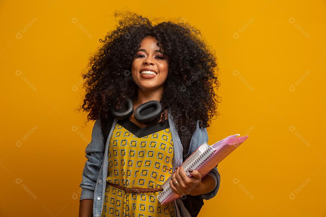 Aluna no campus com livros nos braços. Fundo amarelo.