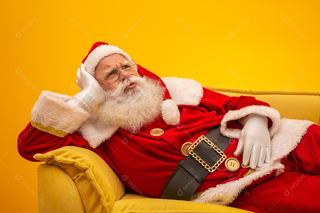 Papai Noel sentado em um sofá amarelo sobre fundo amarelo Sofá amarelo.