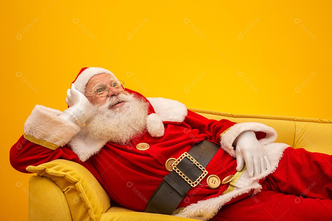Papai Noel sentado em um sofá amarelo sobre fundo amarelo Sofá amarelo.