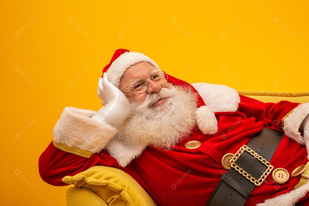 Papai Noel sentado em um sofá amarelo sobre fundo amarelo Sofá amarelo.