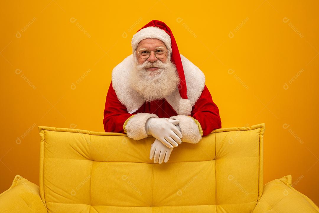 Papai Noel sentado em um sofá amarelo sobre fundo amarelo Sofá amarelo.