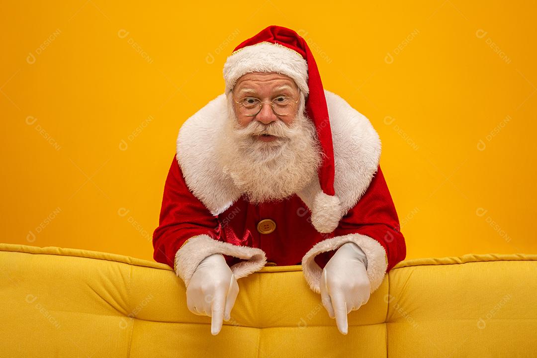 Papai Noel sentado em um sofá amarelo sobre fundo amarelo Sofá amarelo.