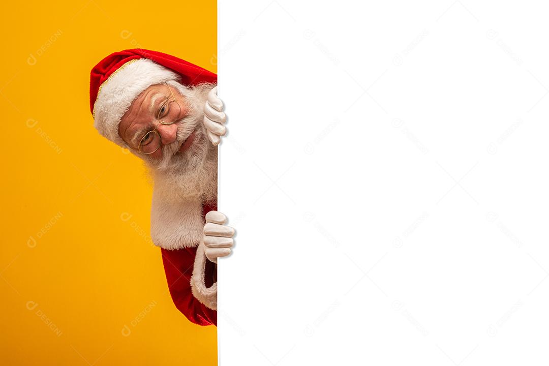 Feliz Papai Noel olhando por trás do sinal em branco isolado em fundo amarelo