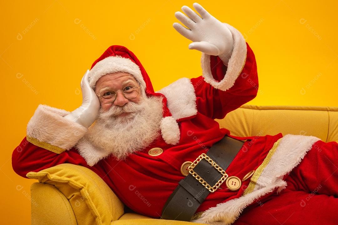Papai Noel sentado em um sofá amarelo sobre fundo amarelo com espaço de cópia. Sofá amarelo.