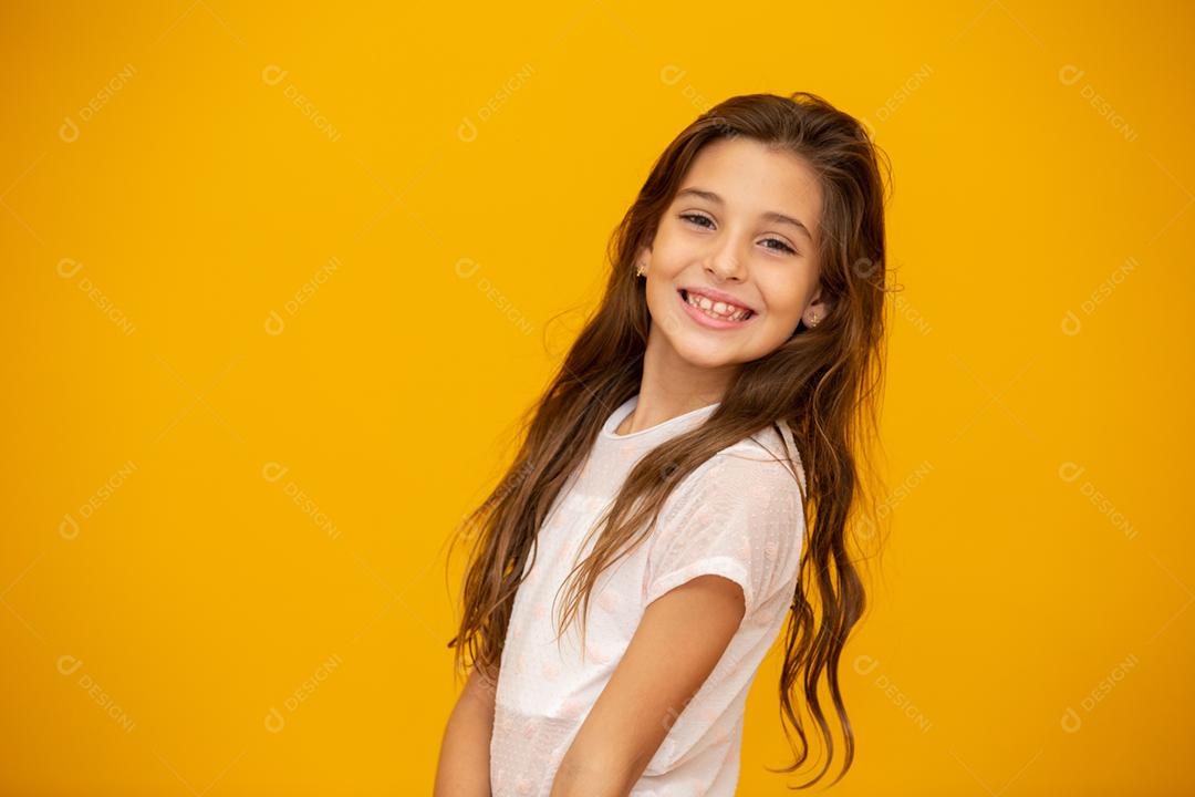 Retrato de uma menina criança sorridente feliz em fundo amarelo.