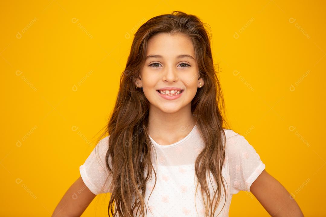 Retrato de uma menina criança sorridente feliz em fundo amarelo.