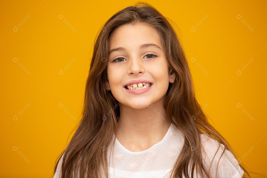 Retrato de uma menina criança sorridente feliz em fundo amarelo.