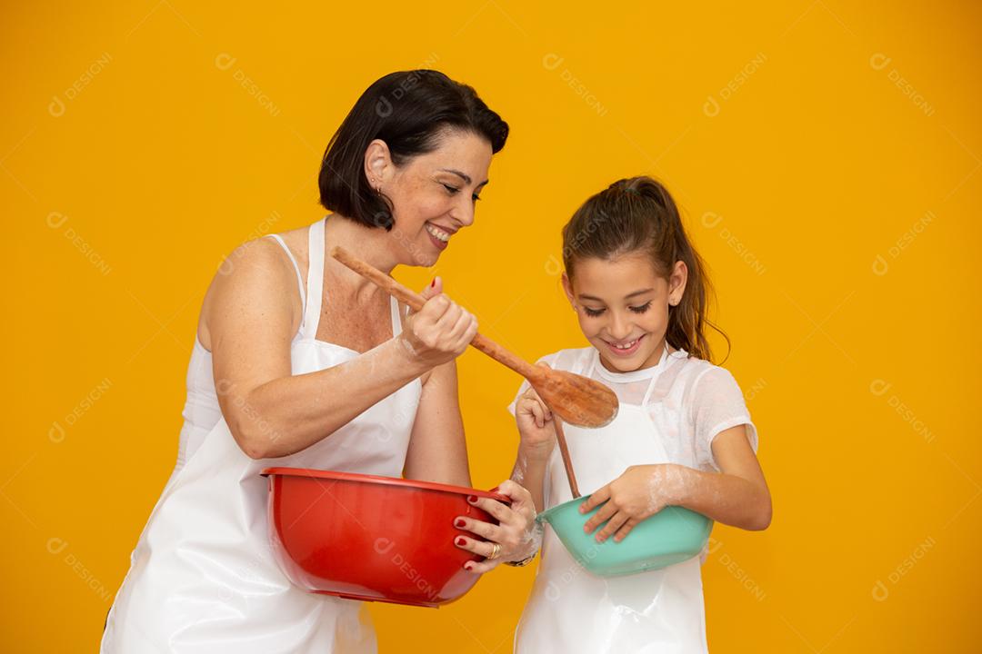 Conceito de dia das mães! Filha e mãe preparando uma receita em fundo amarelo