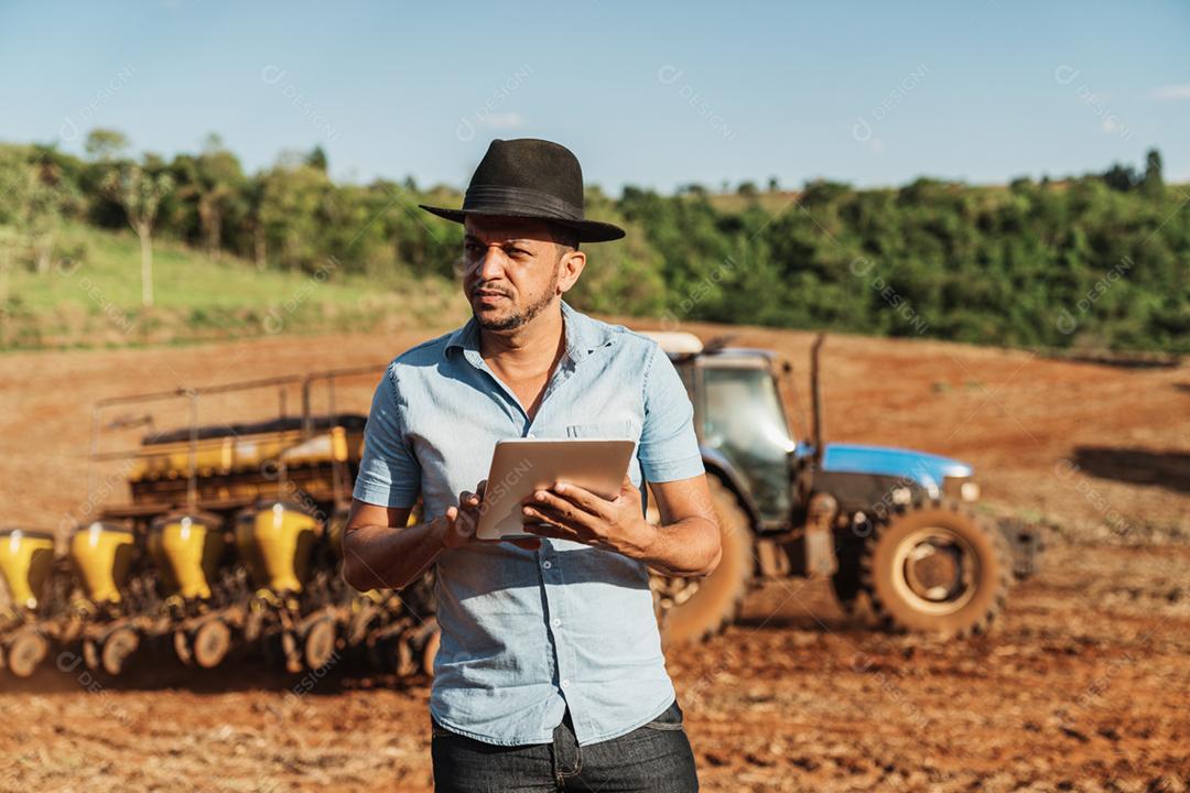 Trabalhador engenheiro usando chapéu com prancheta na mão sobre fundo trator