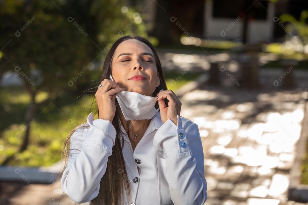 Mulher médica brasileira sorridente em um jaleco branco. Braços cruzados.