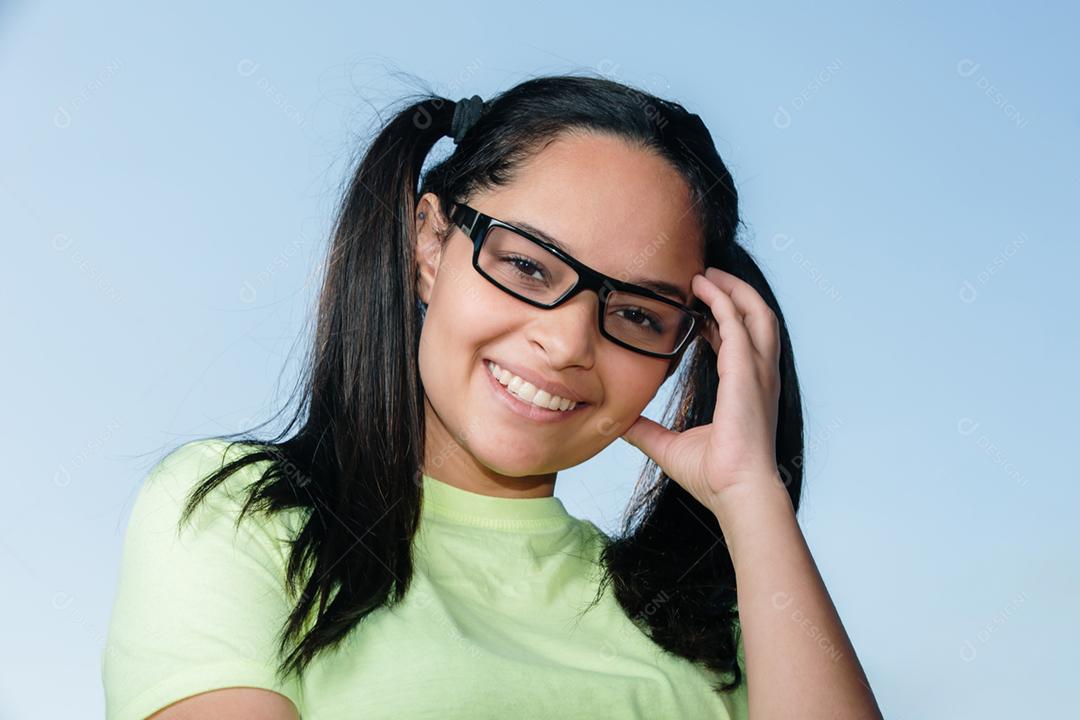 Jovem estudante morena de óculos olhando para a câmera e sorrindo.