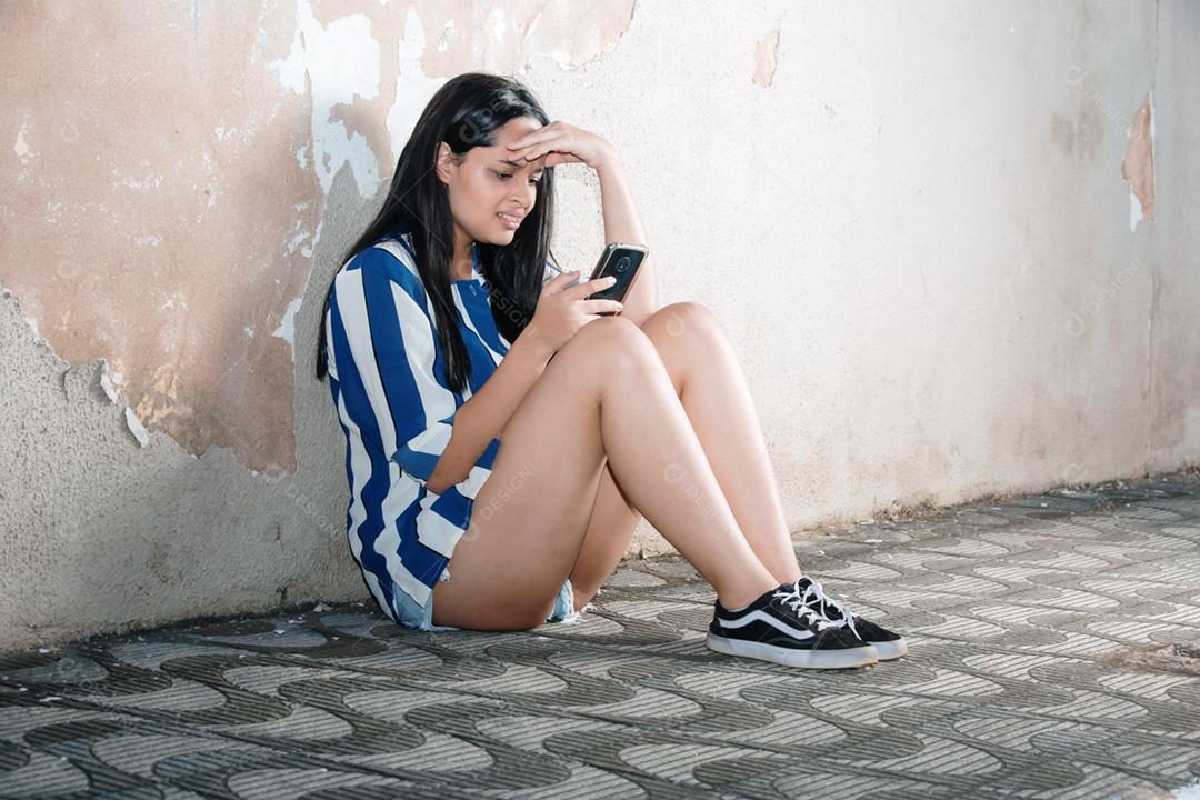 Único adolescente triste segurando um telefone celular lamentando sentado na calçada.