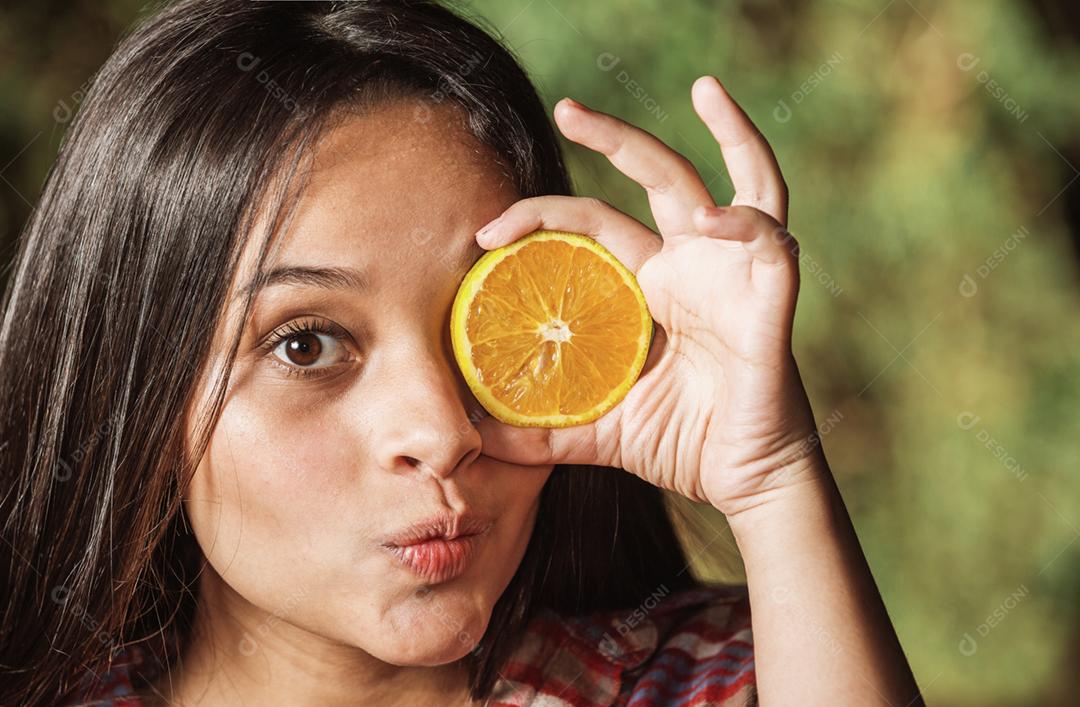 A adolescente cobre parte do rosto com uma laranja. O clima de verão.