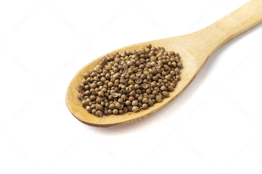 Closeup de sementes de coentro em uma colher de pau isolada sobre fundo branco.