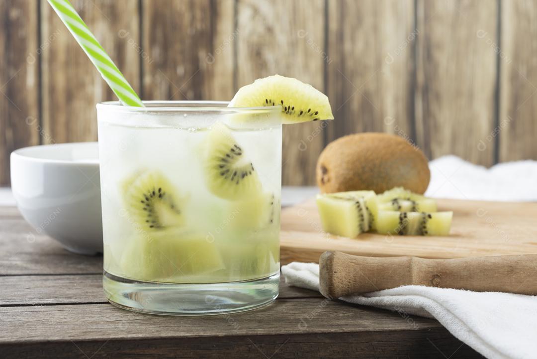 Caipirinha de kiwi brasileiro em um copo com gelo com fatias de frutas sobre placa de madeira.